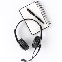 Helpdesk headset with notebook and pen on white desktop. Call center concept. Top view